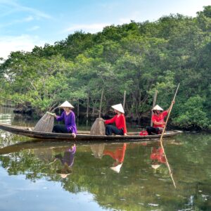 Asian fishermen navigate a river in a wooden boat, surrounded by lush mangroves.