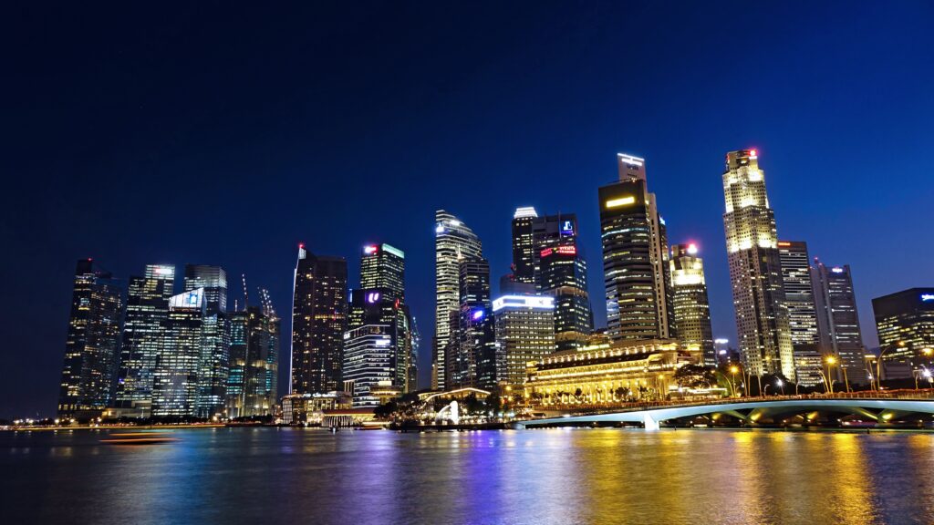 Vibrant night view of Singapore city skyline with illuminated skyscrapers reflected in water.