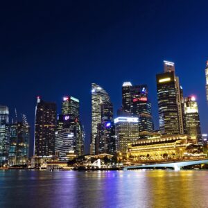 Vibrant night view of Singapore city skyline with illuminated skyscrapers reflected in water.