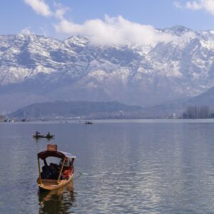 Peaceful view of Dal Lake in Srinagar surrounded by snowcapped Himalayas, featuring traditional boats.