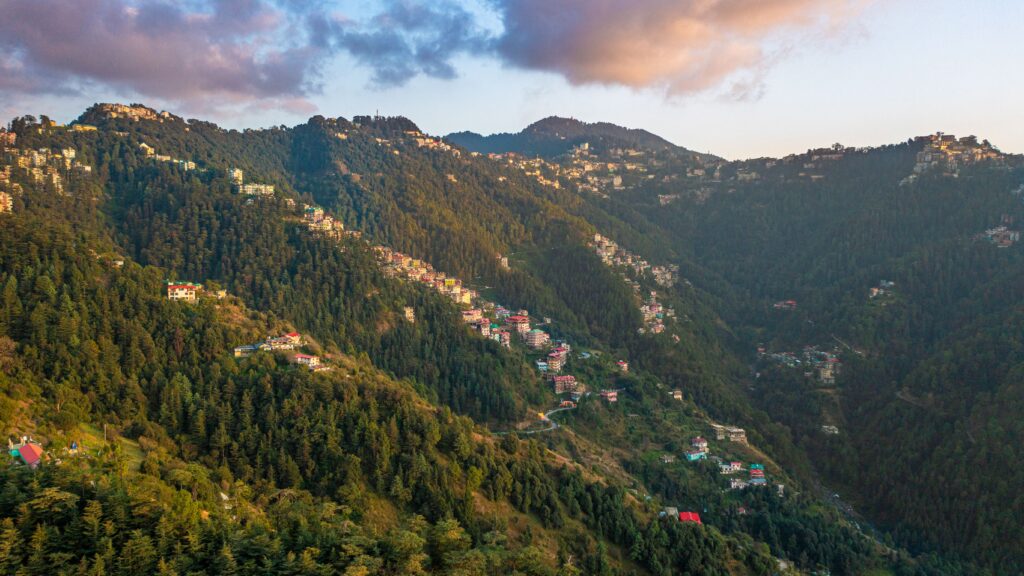 Breathtaking view of Shimla's lush green mountains with scattered houses during sunrise.