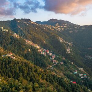 Breathtaking view of Shimla's lush green mountains with scattered houses during sunrise.