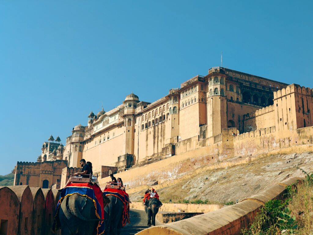 Elephants carrying tourists at historic Amer Fort in Jaipur, India under a clear blue sky.